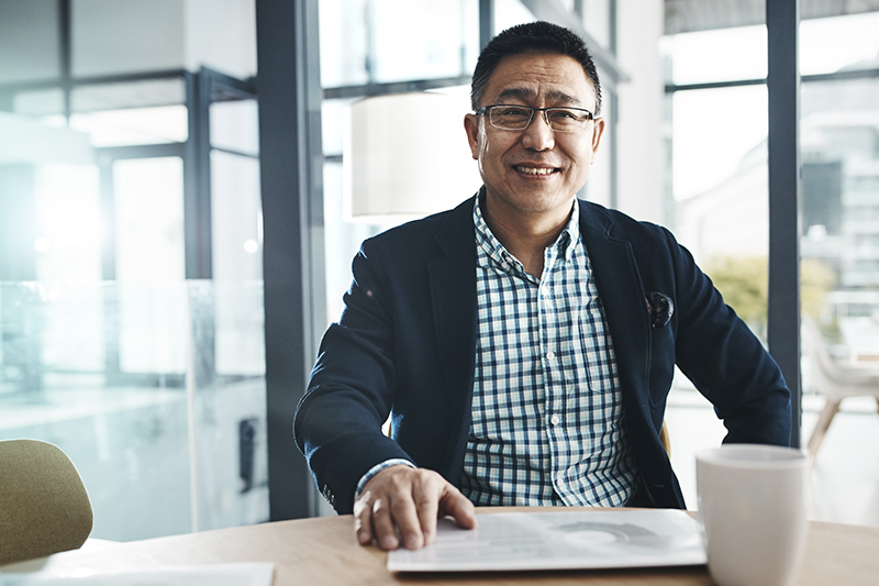 a middle age man sitting at a table with an ipad smiling at the camera