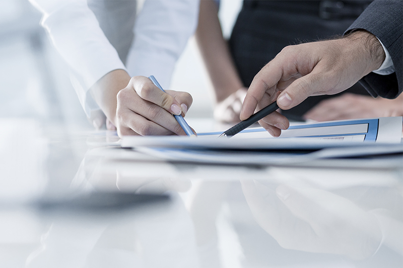 Two hands holding pens on top of a piece of paper