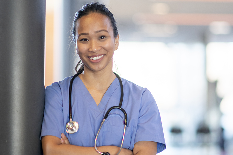 Nurse with a stethoscope leaning on a pole and smiling at the camera