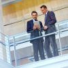 Two men leaning over a balcony, one holding a tablet