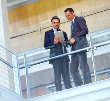 Two men leaning over a balcony, one holding a tablet