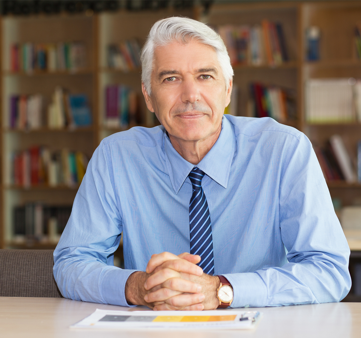 Man sitting at a table with his hands clasped and looking at the camera