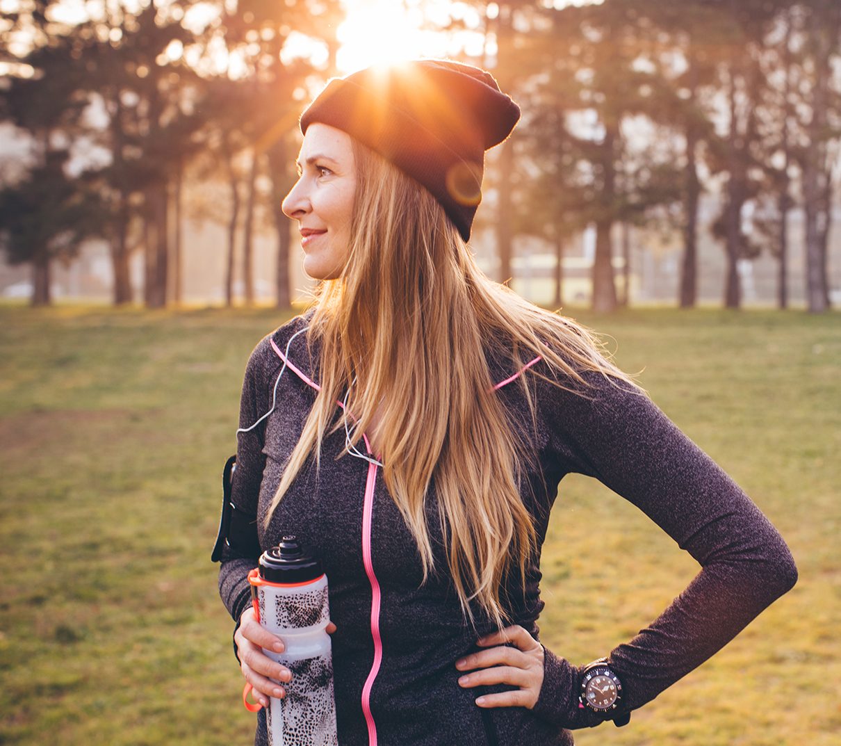 Exercising woman standing still with her hand on her hip and holding a drink bottle